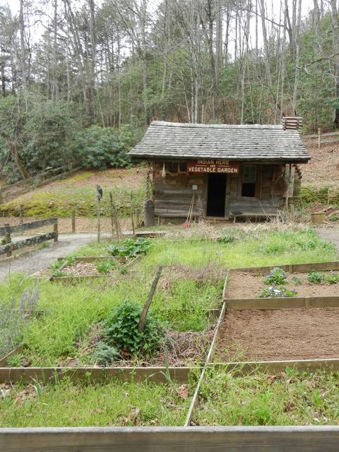 Log cabin with sign "Indian Herb and Vegetable Garden" and foreground raised garden beds
