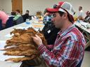 Man in red plaid shirt examining a bundle of dried tobacco leaves in a classroom
