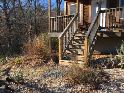 Wooden porch stairs with railing leading to house door; yard with dry, leaf-covered plants.