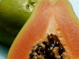 Halved ripe papaya showing orange flesh and black seeds, whole green papaya behind