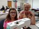Young girl and elderly woman at a Janome sewing machine in a community room