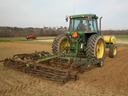 Green tractor pulling a cultivator across a bare plowed field