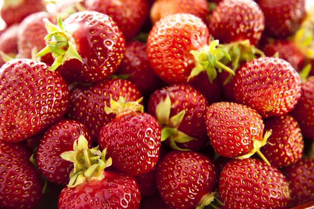 Close-up of multiple ripe red strawberries with green calyxes and seeds visible