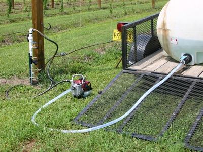 White water tank on trailer connected by hose to a small pump and field water spigot