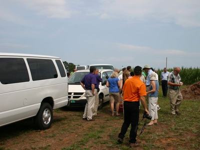 Group of people gathered beside white vans on a grassy field