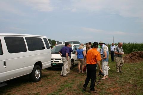 Group of people gathered beside white vans on a grassy field