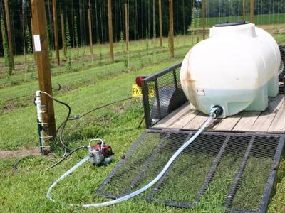 White water tank on trailer with hose and pump connected, beside trellised field