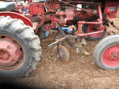 Red tractor with attached disc harrow tilling dry, churned soil