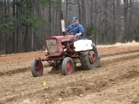Man driving red tractor plowing furrows in a bare field