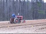 Person driving a red tractor across a plowed field with bare trees in the background