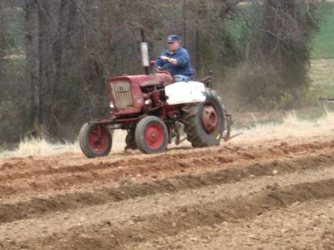 Person driving a red tractor across a freshly plowed field