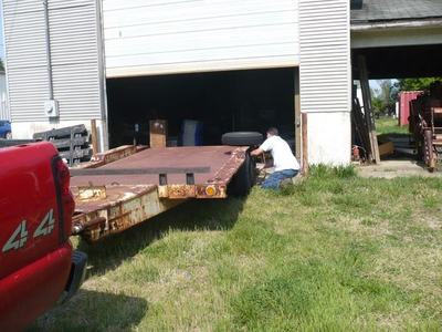 Man kneeling beside rusted flatbed trailer being moved into open garage