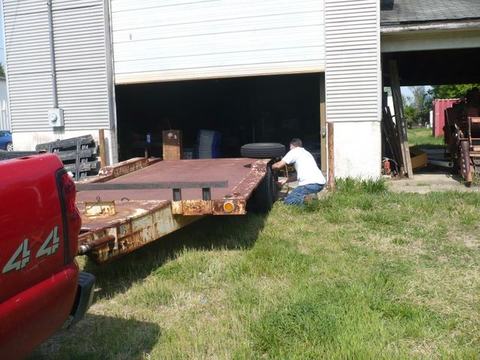 Man kneeling beside rusted flatbed trailer being moved into open garage