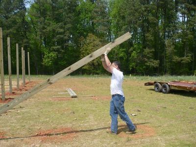 Man lifting a long wooden post upright at an outdoor construction site