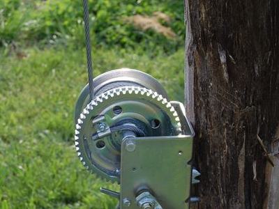 Hand crank winch mounted on a wooden post with steel cable attached
