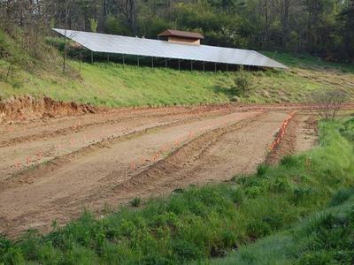 Plowed field with orange marker flags below a hillside solar panel array and small shed