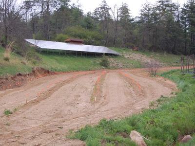 Solar panel array on hillside above cleared, staked planting rows in a dirt field