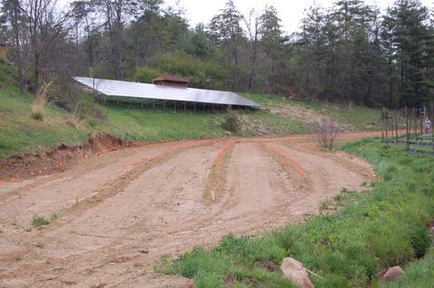Solar panel array on hillside above cleared, staked planting rows in a dirt field