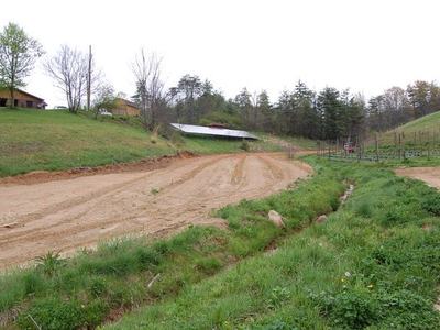 Graded dirt road curving through grassy hillside toward a low barn and houses in distance