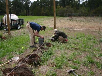 Two workers kneel and bend installing irrigation tubing in a grassy field