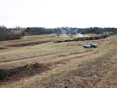 White pickup truck beside long covered rows of drying racks on a grassy field