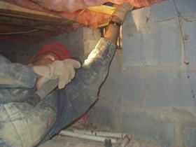 Pulling back insulation in a crawlspace to look for signs of termite activity.