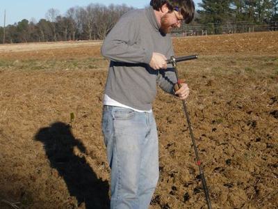 Man wearing sweater inserting a soil probe into a plowed field