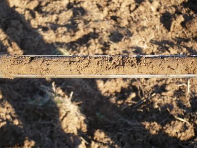 Metal beam coated with a strip of dried soil suspended over tilled dirt