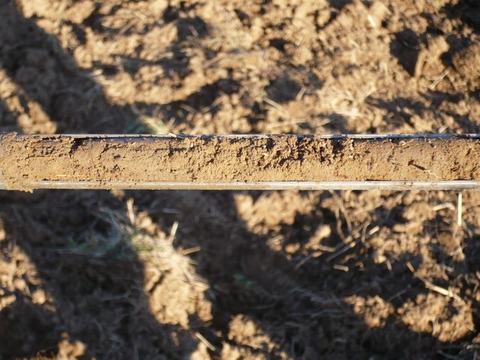 Metal beam coated with a strip of dried soil suspended over tilled dirt