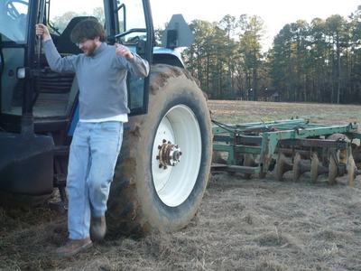 Man stepping down from tractor beside rear tire and disc harrow in a field