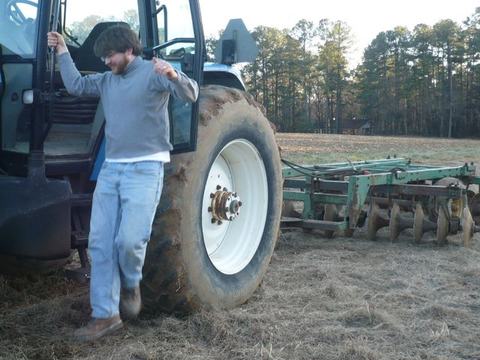 Man stepping down from tractor beside rear tire and disc harrow in a field