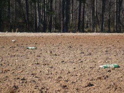 Plowed field with three green bags scattered across it and a tree line beyond
