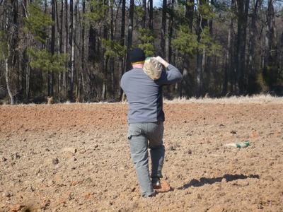 Man carrying a burlap sack over his shoulder across a plowed field toward trees