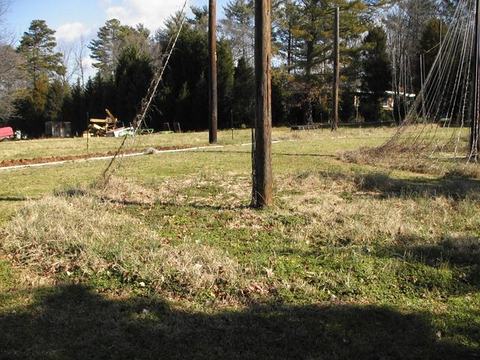 Wooden utility pole standing in a grassy vacant lot with trees and equipment behind