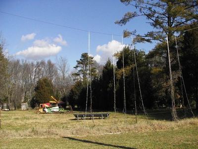 Field with long ropes hanging from an overhead wire and a round trampoline nearby