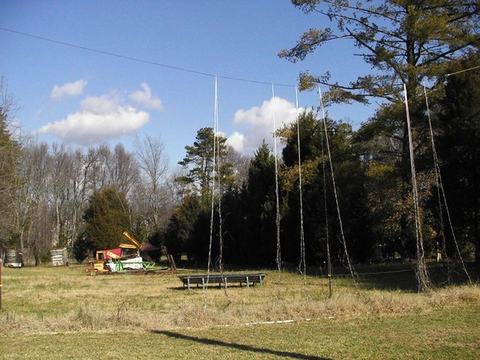 Field with long ropes hanging from an overhead wire and a round trampoline nearby