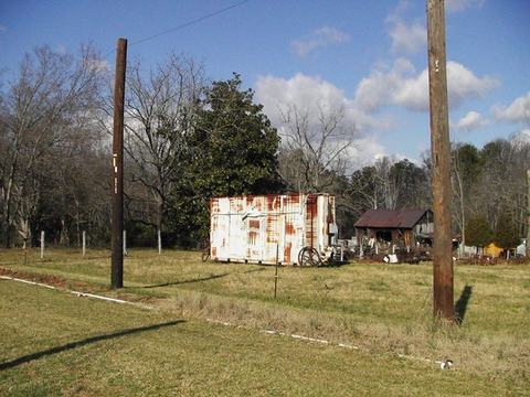 Rusty white shipping container and wagon wheels in grassy field near small shed and utility poles