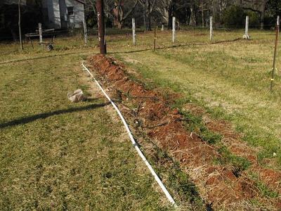 Long shallow trench with exposed soil and a white PVC pipe in a grassy yard