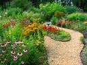 Gravel path curving through colorful flower beds with a small birdbath ahead
