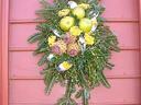 Evergreen wreath with green apples and yellow flowers hung on pink paneled door