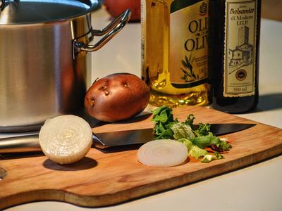 Cutting board with onion and potato. Olive oil bottles in the background. 