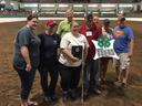 Eight people in an indoor arena holding a 4‑H clover award and a plaque
