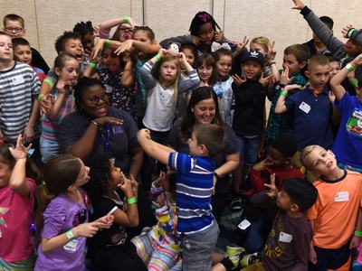 Group of children and two adults making faces and hand gestures in a crowded room