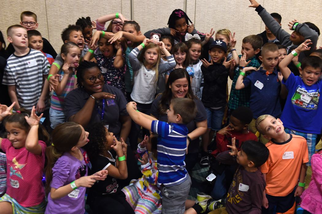 Group of children and two adults making faces and hand gestures in a crowded room