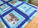Blue and teal patchwork quilt with horse photo panels and a blue ribbon on a wooden table