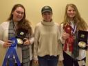 Three people standing; outer two hold belt-buckle awards and ribbons reading "North Carolina 4‑H"