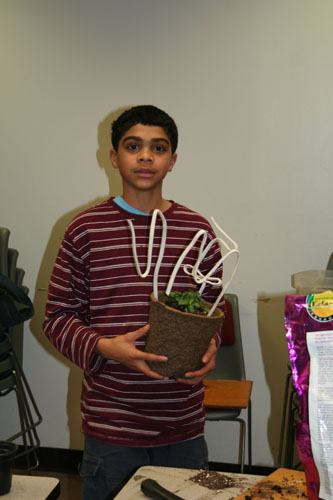 Young person holding a potted plant with white wire supports indoors
