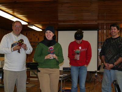 Four adults standing indoors holding small sock puppets; left sweatshirt reads "Michigan."