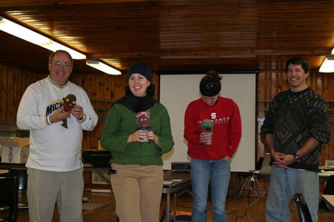 Four adults standing indoors holding small sock puppets; left sweatshirt reads "Michigan."