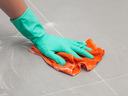 Hand in green rubber glove scrubbing gray tile floor with orange cloth